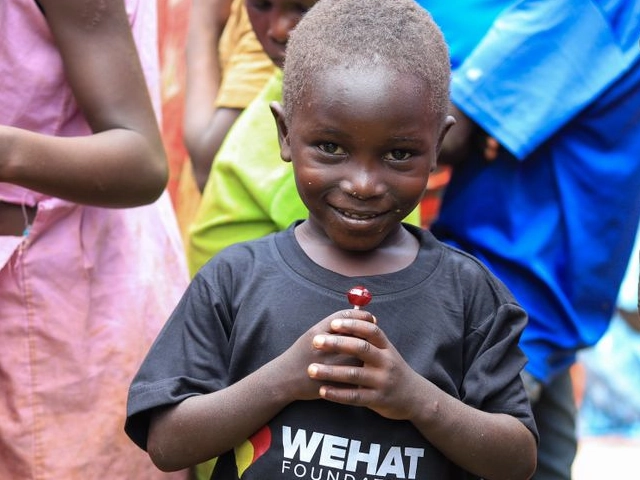 young boy wearing a black t-shirt with the wehat foundation logo holding a lolipop and smiling